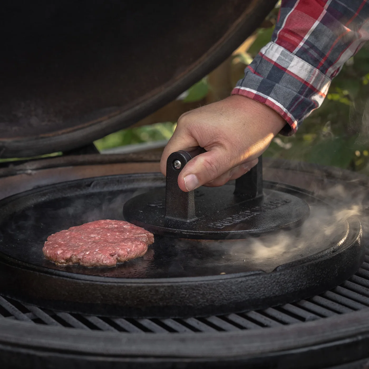 Hand pressing a burger patty on a grill