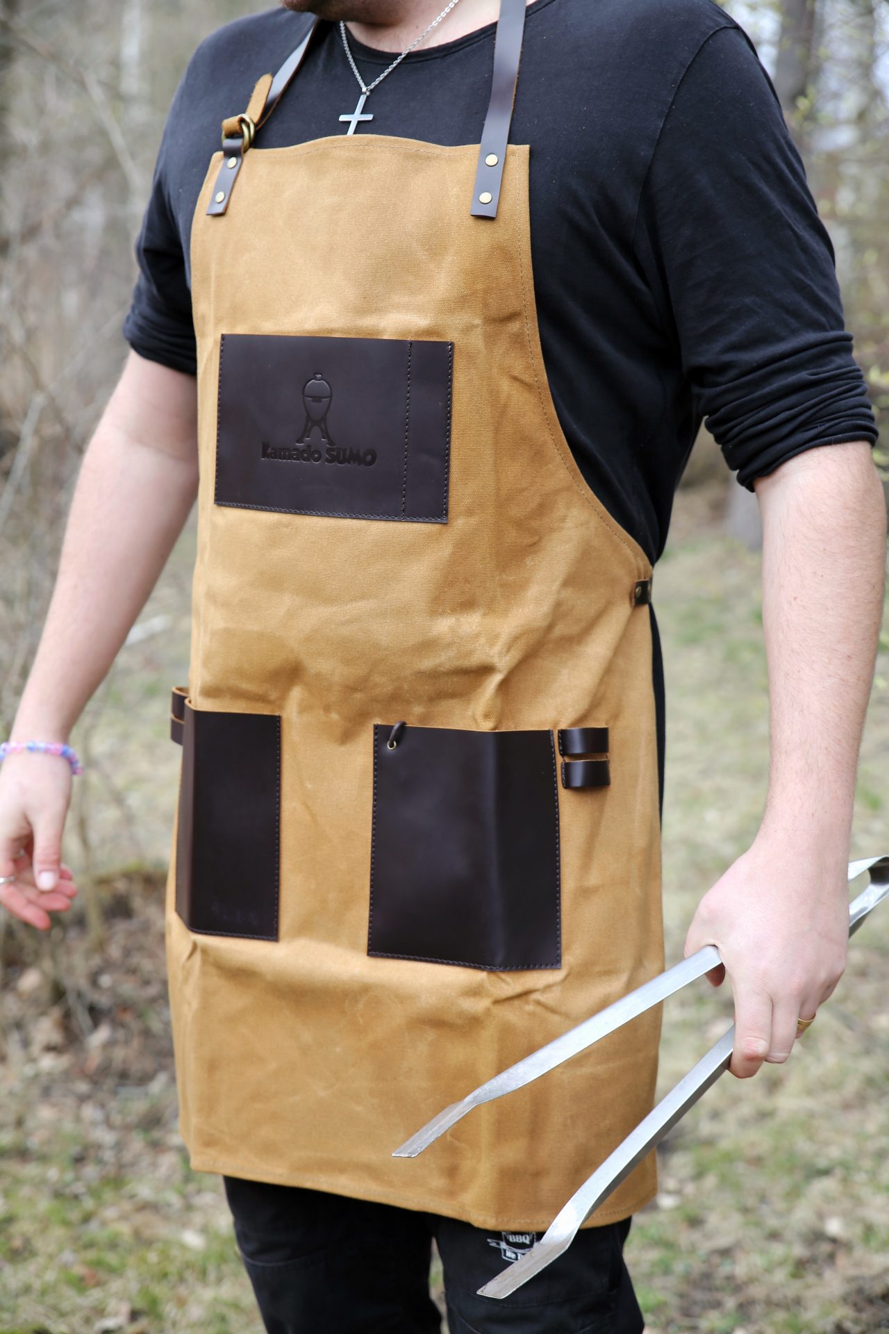Person wearing a Kamado Sumo grilling apron with tongs