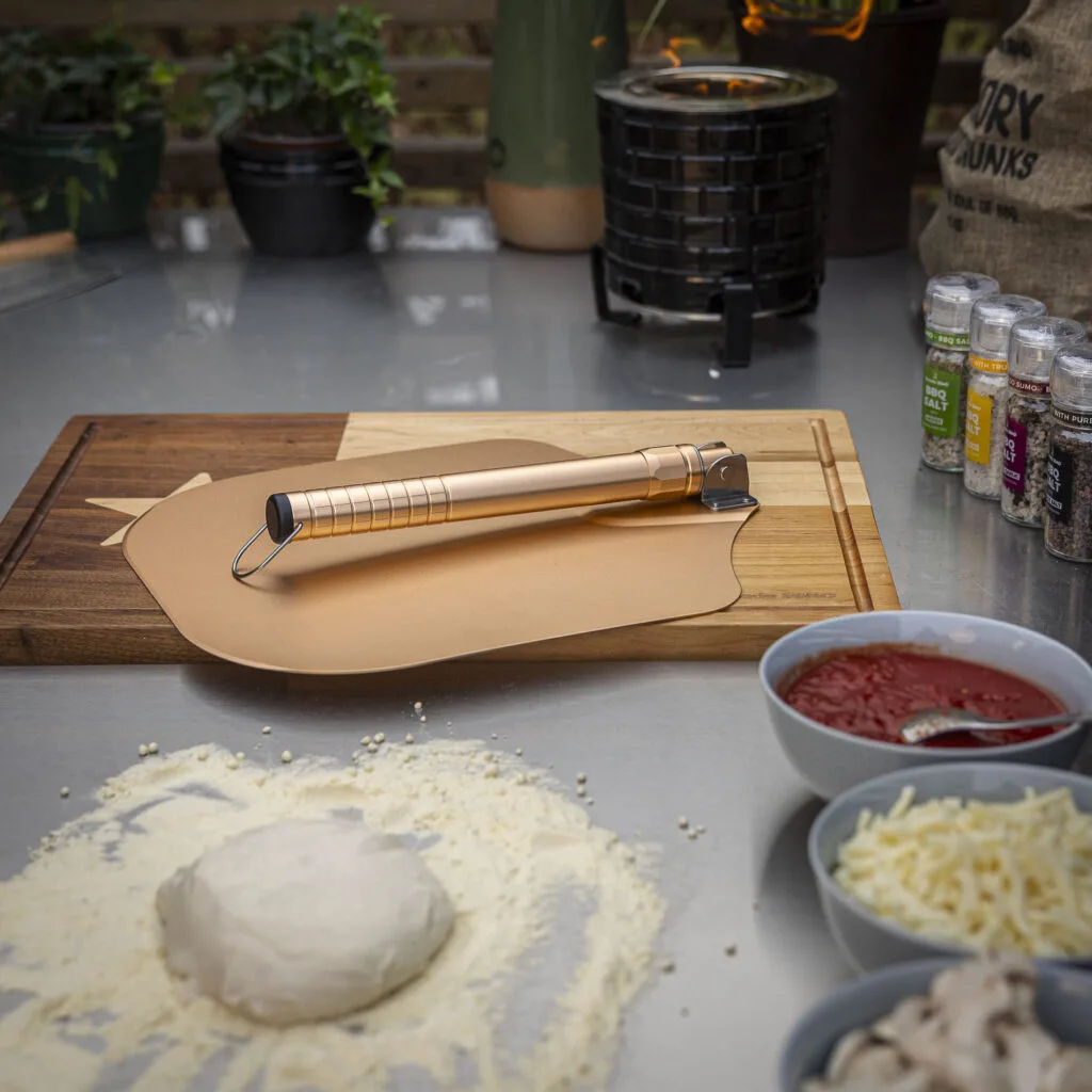 Golden pizza peel on a wooden cutting board with pizza ingredients