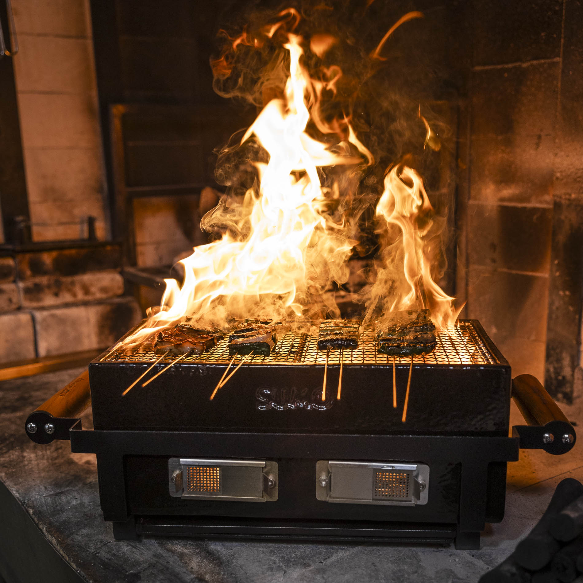 Kamado Sumo ceramic grill with flames and skewers cooking