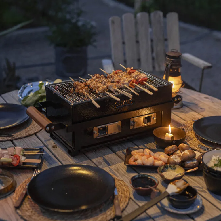 Kamado Sumo ceramic grill with skewers cooking outdoors at night