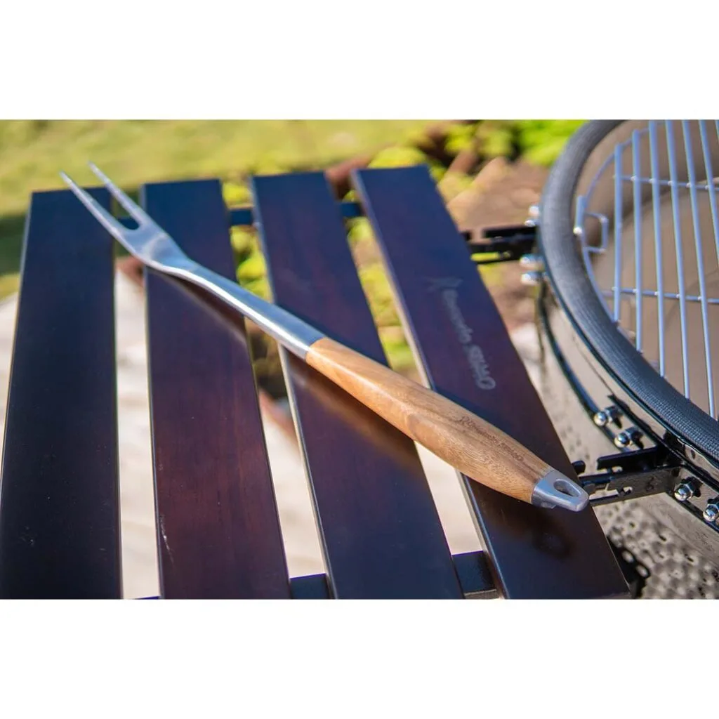 Stainless steel grilling fork with wooden handle on a grill shelf