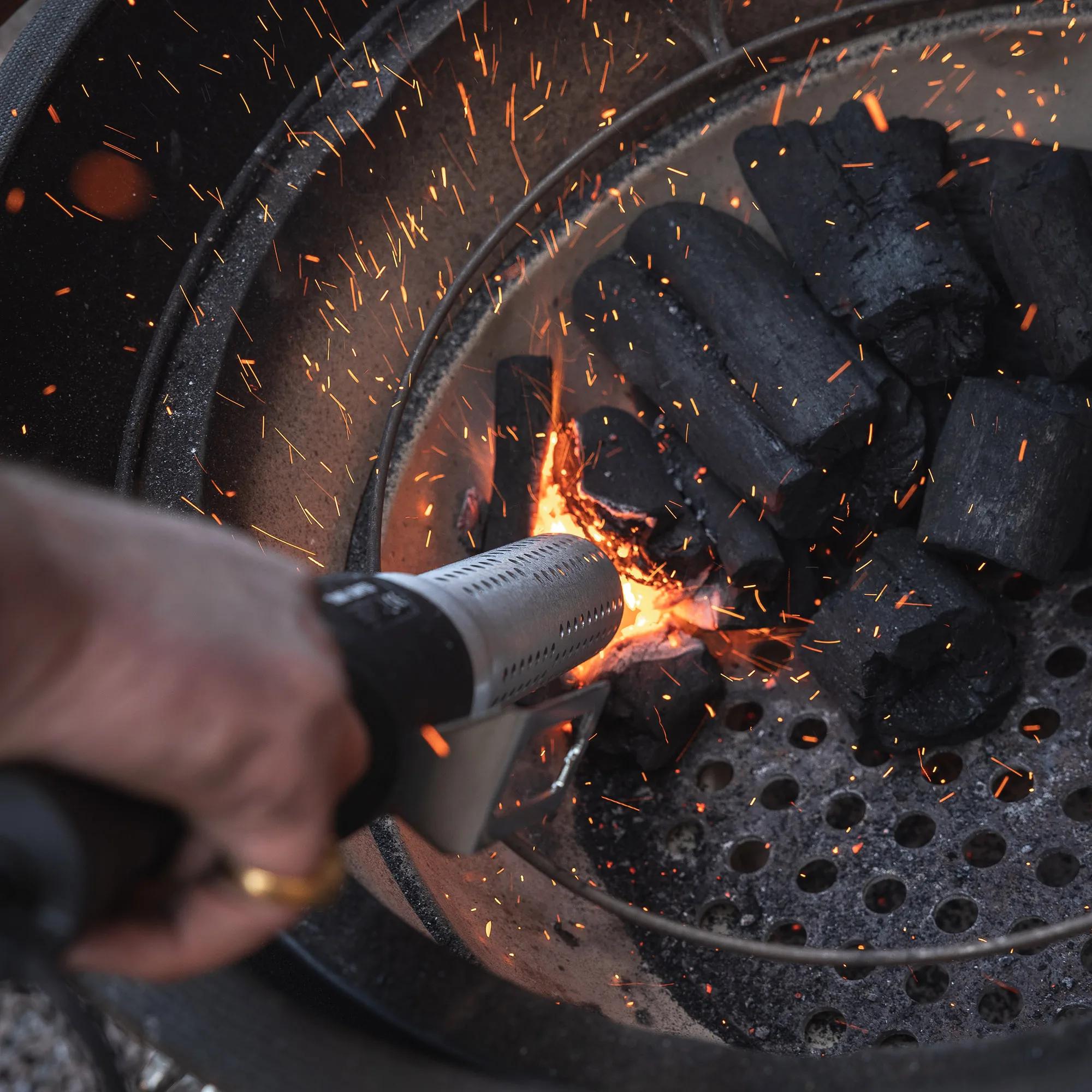 Handheld lighter igniting charcoal in a grill