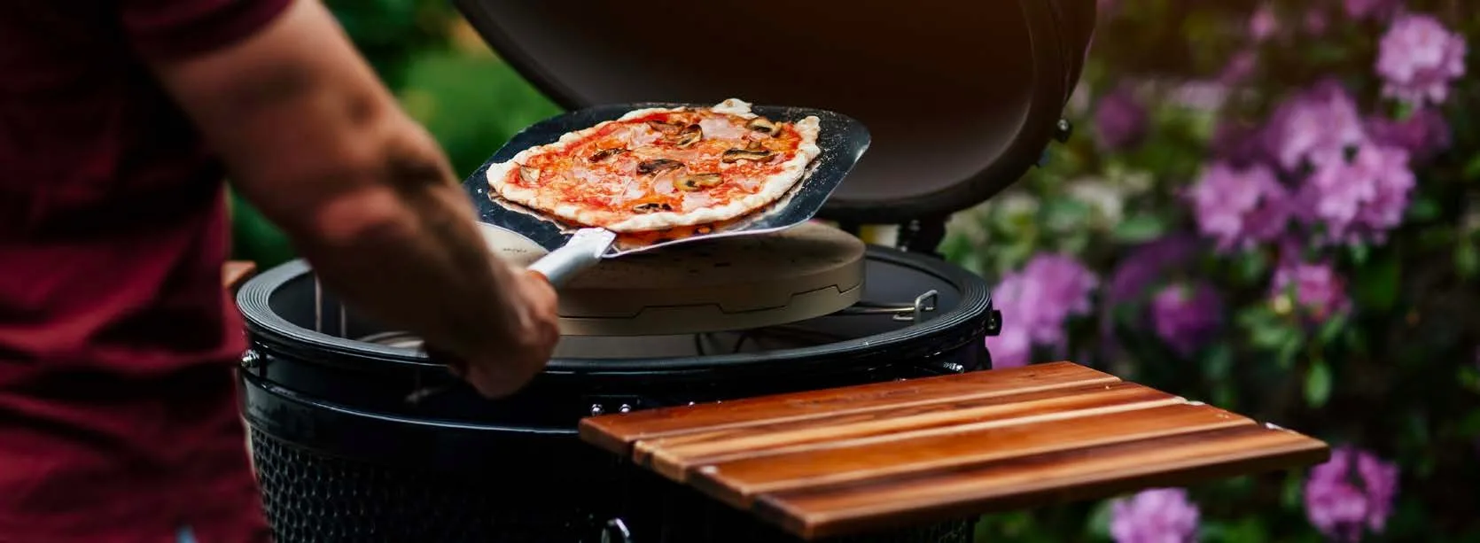 Person using a pizza peel to remove a pizza from a Kamado Sumo grill